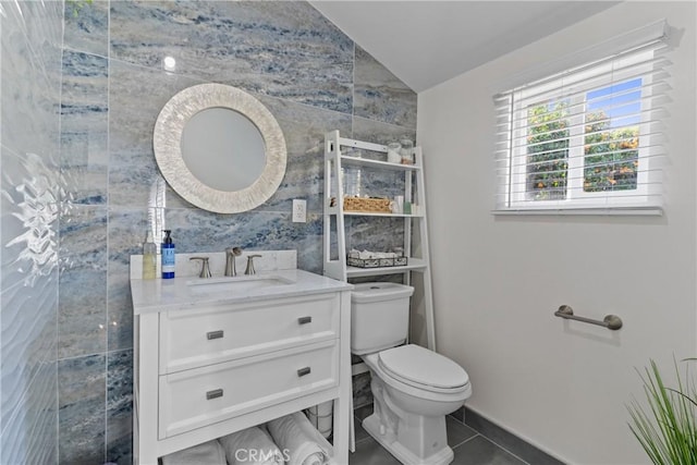 half bath featuring toilet, lofted ceiling, tile patterned floors, vanity, and tile walls