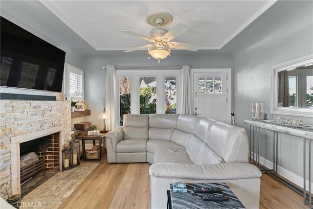 living room featuring light wood-style floors, ceiling fan, and a stone fireplace