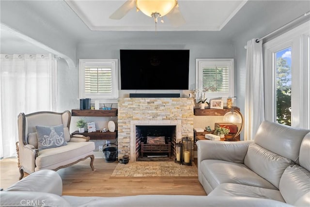 living room with ceiling fan, a tray ceiling, a fireplace, and wood finished floors