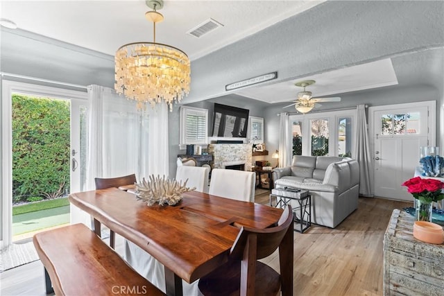 dining area with a textured ceiling, ceiling fan with notable chandelier, a fireplace, visible vents, and light wood-style floors