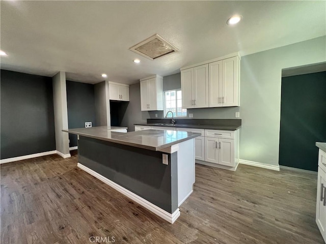 kitchen featuring dark wood-type flooring, a sink, white cabinets, and a center island