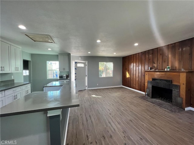 unfurnished living room featuring a fireplace with flush hearth, wooden walls, a wealth of natural light, and wood finished floors