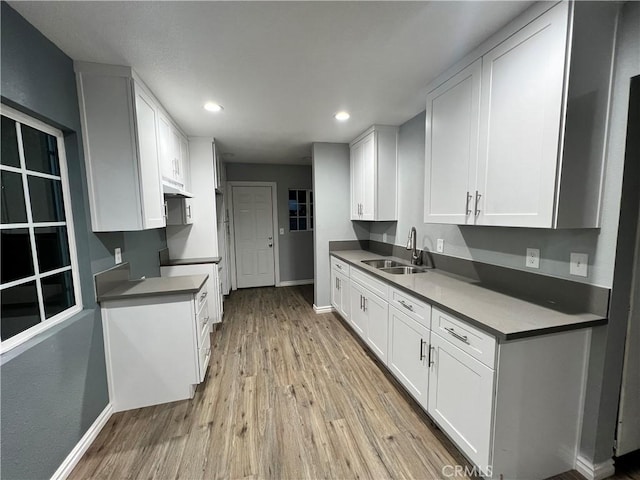 kitchen with recessed lighting, a sink, white cabinets, light wood-type flooring, and dark countertops