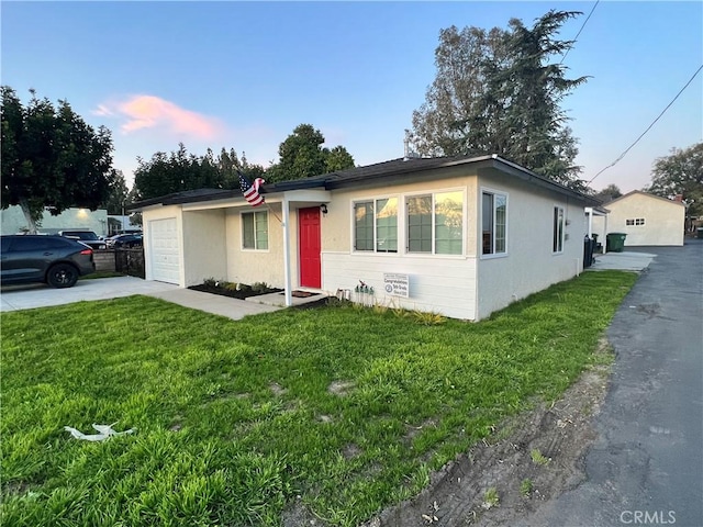 single story home featuring an attached garage, a front lawn, concrete driveway, and stucco siding