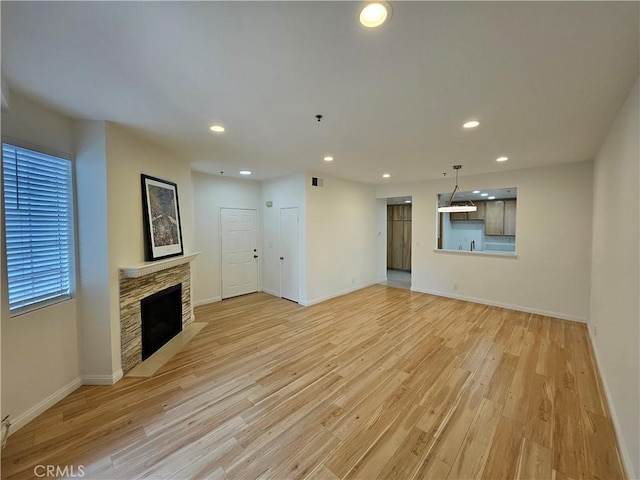 unfurnished living room featuring recessed lighting, a stone fireplace, and light wood finished floors