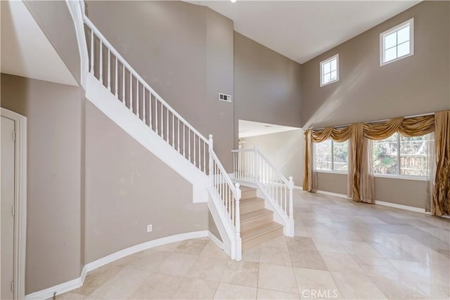 stairs featuring tile patterned flooring, a high ceiling, visible vents, and baseboards