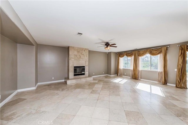 unfurnished living room featuring ceiling fan, a tiled fireplace, visible vents, and baseboards