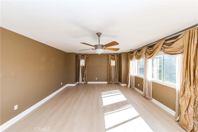 spare room with light wood-type flooring, a ceiling fan, and baseboards