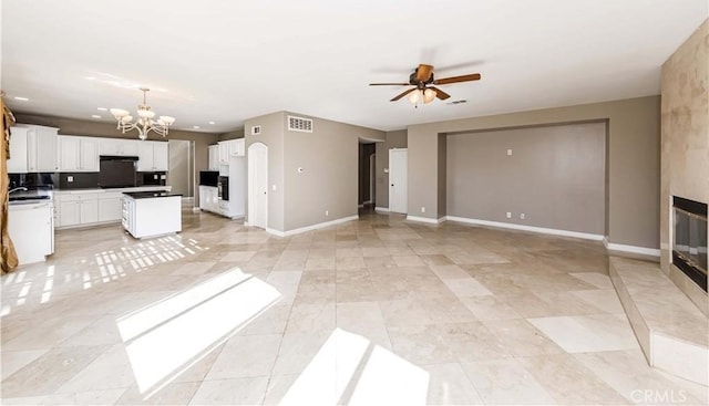 unfurnished living room featuring a large fireplace, baseboards, visible vents, and ceiling fan with notable chandelier