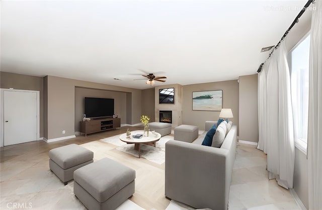 living area with a large fireplace, ceiling fan, and baseboards