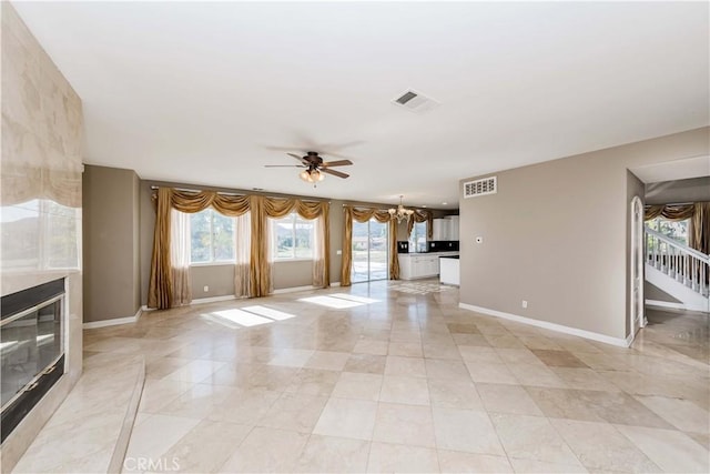 unfurnished living room with baseboards, stairs, visible vents, and ceiling fan with notable chandelier