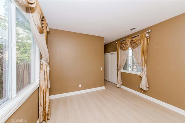 unfurnished room with light wood-style floors, visible vents, and baseboards