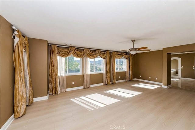 unfurnished room featuring arched walkways, a ceiling fan, light wood-style flooring, and baseboards