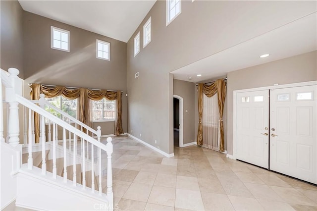 entrance foyer with a towering ceiling, light tile patterned flooring, stairway, and baseboards