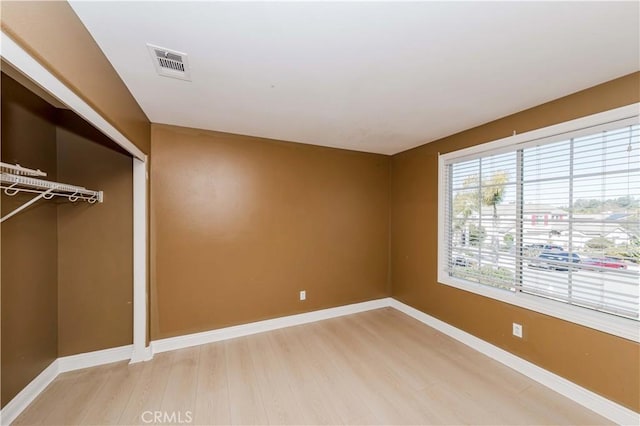 unfurnished bedroom with a closet, visible vents, baseboards, and wood finished floors