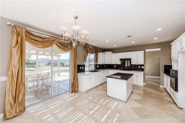 kitchen with dark countertops, white cabinets, a sink, and under cabinet range hood