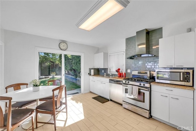 kitchen with light countertops, wall chimney exhaust hood, tasteful backsplash, appliances with stainless steel finishes, and white cabinetry