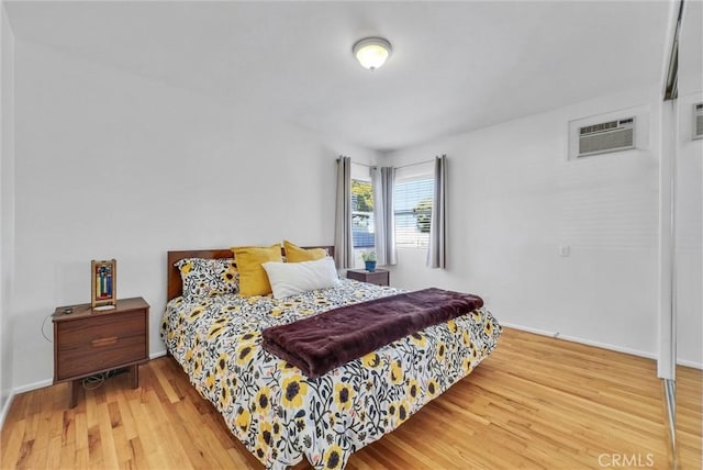 bedroom with baseboards, a wall mounted AC, and wood finished floors