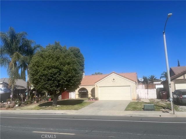 view of front of property with an attached garage, fence, a tile roof, driveway, and stucco siding