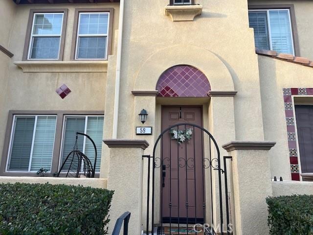 view of exterior entry featuring a gate and stucco siding