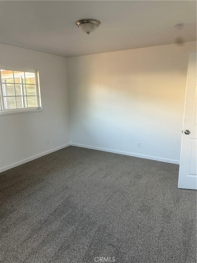 unfurnished room featuring baseboards and dark carpet