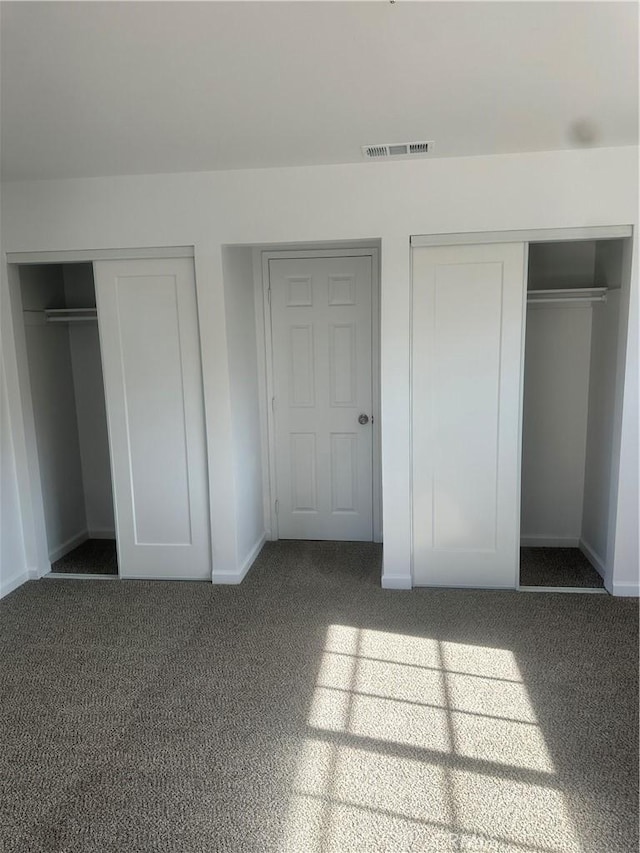 unfurnished bedroom featuring baseboards, visible vents, dark carpet, and two closets