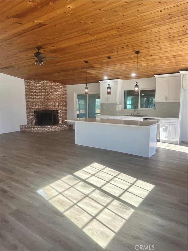 kitchen featuring wood ceiling, open floor plan, decorative light fixtures, white cabinetry, and a sink