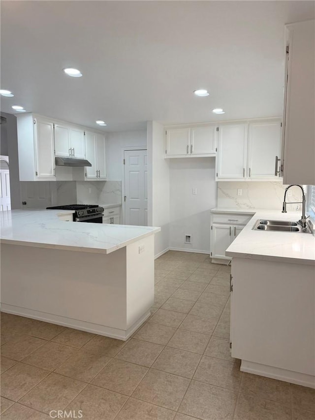 kitchen with white cabinets, a sink, a peninsula, gas range, and under cabinet range hood