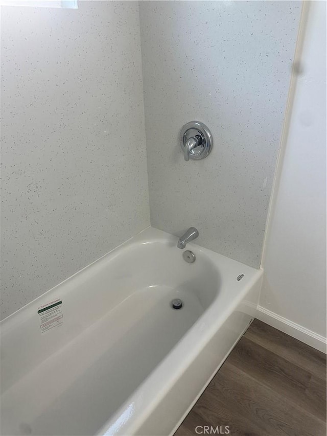 full bath featuring a tub to relax in, wood finished floors, and baseboards