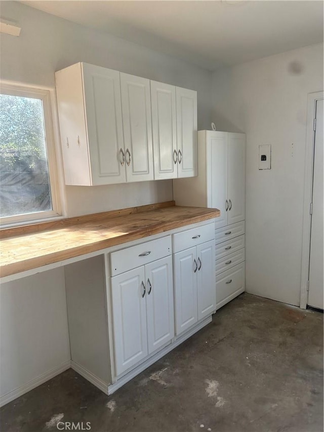 kitchen with butcher block countertops, white cabinets, and concrete flooring