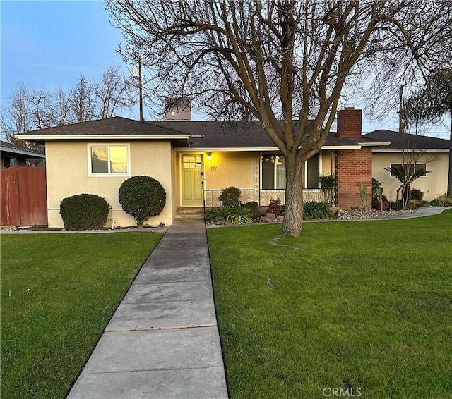 ranch-style home with a chimney, a front yard, fence, and stucco siding