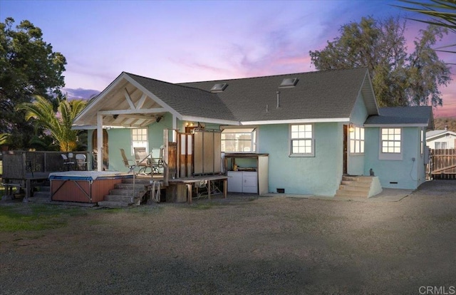 rear view of house featuring a shingled roof, fence, a hot tub, and stucco siding