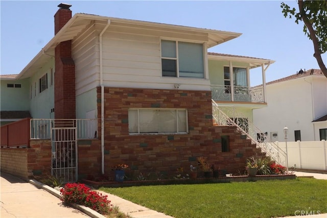 view of front facade featuring fence, stone siding, stairway, a front yard, and a chimney