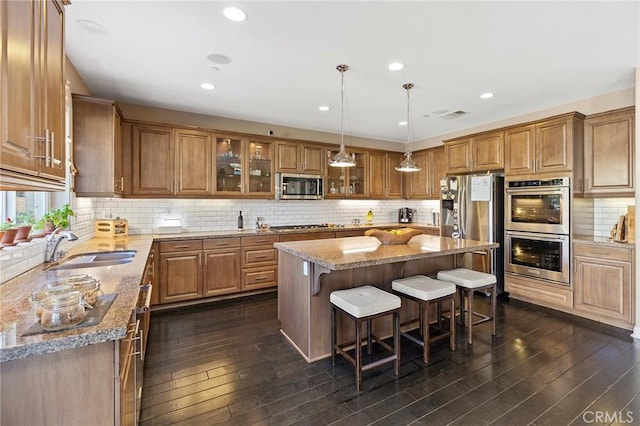 kitchen featuring brown cabinetry, a kitchen island, glass insert cabinets, appliances with stainless steel finishes, and a sink