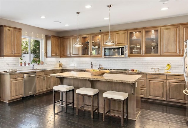 kitchen featuring glass insert cabinets, appliances with stainless steel finishes, brown cabinetry, and a center island