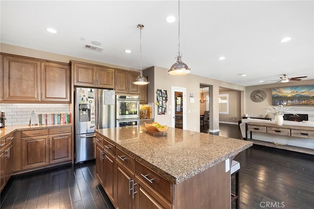 kitchen with light stone counters, a kitchen island, visible vents, appliances with stainless steel finishes, and pendant lighting