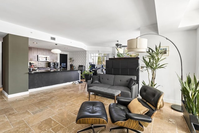 living room with stone tile flooring, visible vents, a ceiling fan, and baseboards