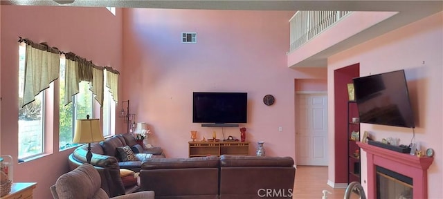 living area featuring a glass covered fireplace, visible vents, a towering ceiling, and light wood finished floors