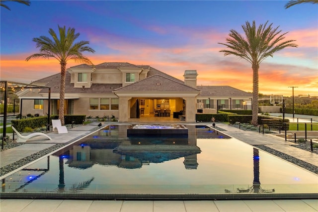 pool at dusk with a patio area and an outdoor pool