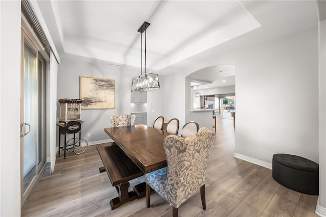 dining room featuring arched walkways, a tray ceiling, wood finished floors, and baseboards