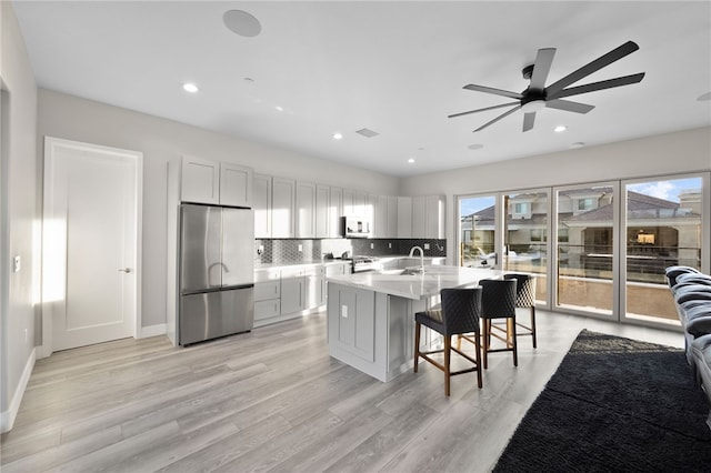 kitchen with an island with sink, a breakfast bar area, stainless steel refrigerator, open floor plan, and white cabinetry