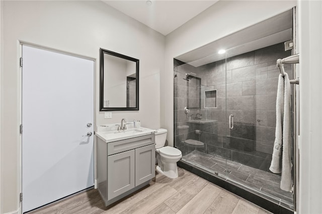 bathroom with toilet, vanity, a shower stall, and wood finished floors