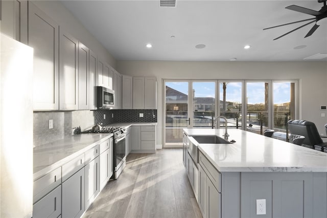 kitchen featuring gray cabinetry, a sink, appliances with stainless steel finishes, backsplash, and light wood finished floors