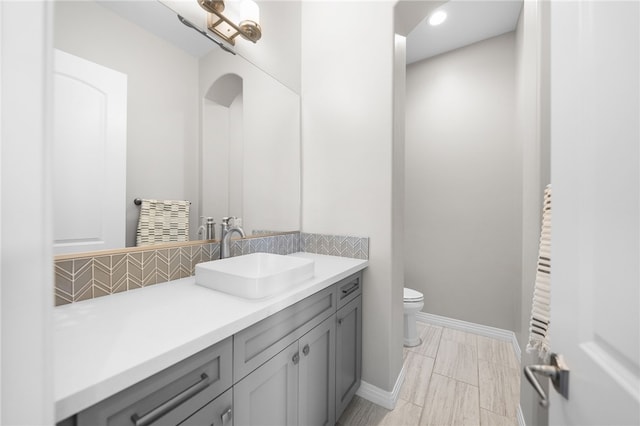 bathroom featuring toilet, tasteful backsplash, baseboards, and vanity