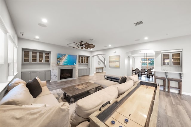 living room featuring light wood finished floors, visible vents, arched walkways, a fireplace, and recessed lighting