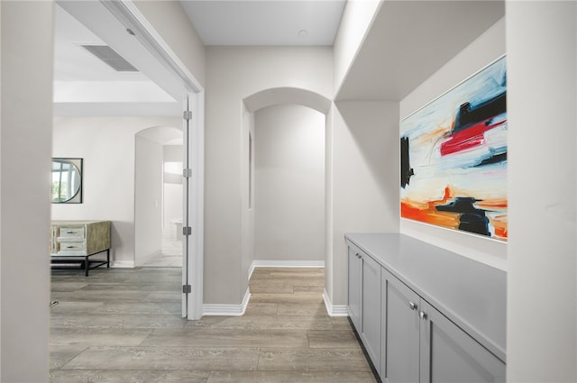 corridor featuring light wood-type flooring, visible vents, arched walkways, and baseboards