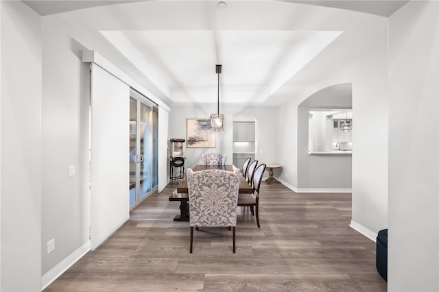 dining space featuring arched walkways, baseboards, a raised ceiling, and wood finished floors