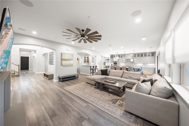 living room with arched walkways, light wood-style flooring, recessed lighting, a ceiling fan, and baseboards