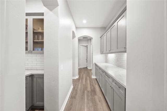 bar with light wood-style floors, arched walkways, baseboards, and tasteful backsplash