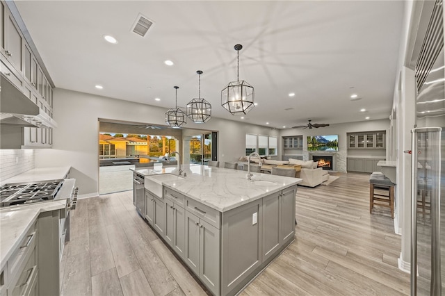 kitchen featuring pendant lighting, open floor plan, an island with sink, and gray cabinetry